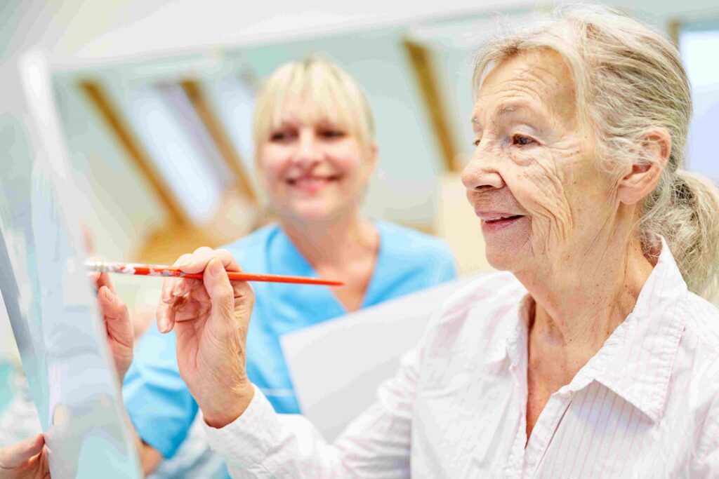 Alzheimer e terapie non farmacologiche. Anziana signora dipinge con l'assistenza di una caregiver